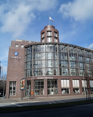 Zweistöckiges Gebäude mit einer modernen Glasfassade, beschriftet mit "ZÜRICH" und "srh Campus Hamburg". Eine Fahne weht oben auf dem Turm.