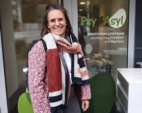 Frau mit Brille und Schal steht vor dem Eingang des Psychiatrie- und Migrationszentrums "Psy 4 Asyl".