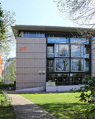 Moderne Gebäude mit großen Fenstern und einem klaren Design, umgeben von Bäumen und einer grünen Fläche. Das Logo "srh" ist an der Fassade sichtbar.