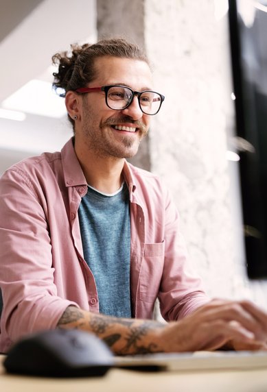 Junger Mann mit Briller und Hemd sitzt vor dem Computer und optimiert eine Webseite